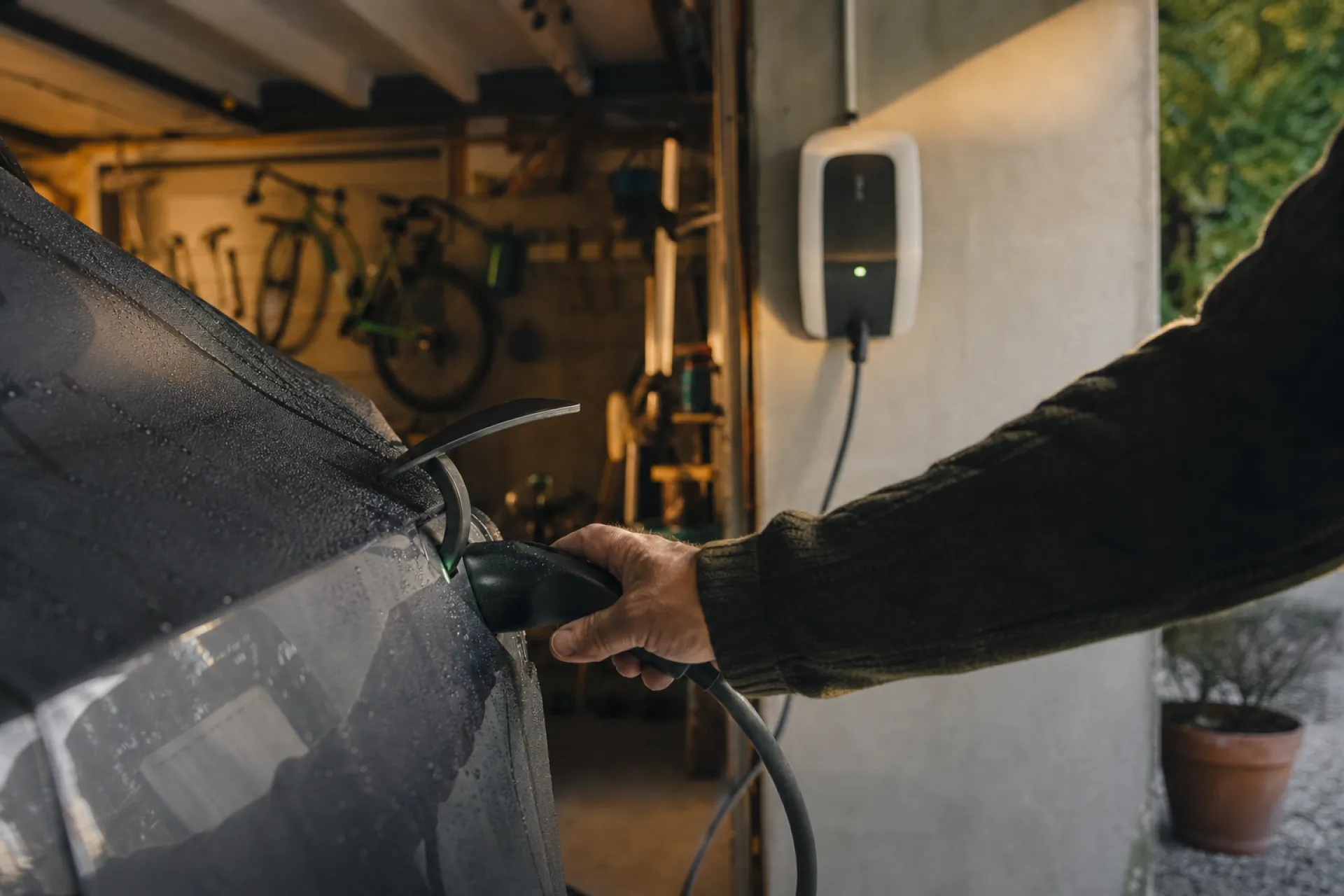 Main branchant le câble de recharge d'une voiture électrique dans un garage équipé d'une borne murale
